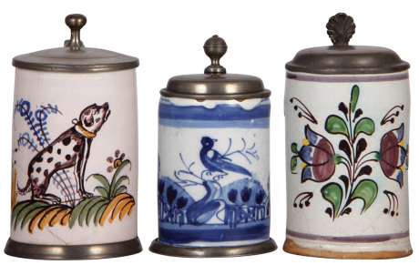 Three Faience steins, 5.7" ht. to 6.2" ht., late 1700s, Nürnberger Walzenkrug & two others, all have pewter lids, first two have pewter footrings, first has a 2" hairline bottom front & a later lid, second has three tight 2" lines & upper rim chips, third